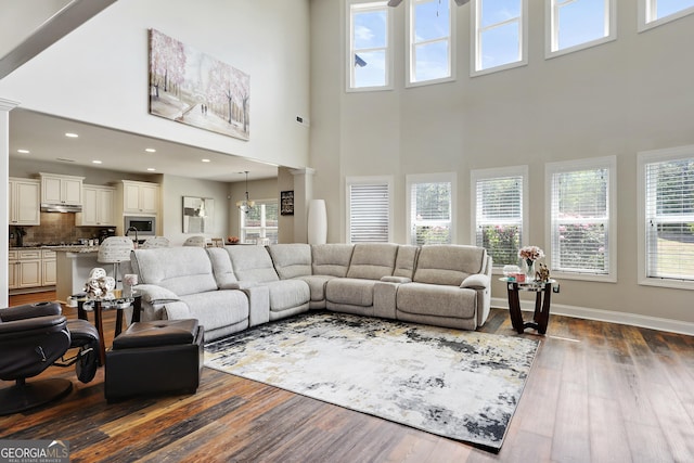 living room with dark hardwood / wood-style floors, a towering ceiling, and decorative columns