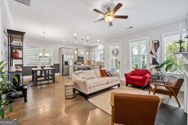 living room with crown molding, ceiling fan with notable chandelier, and light hardwood / wood-style floors