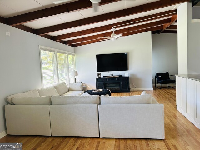 living room with ceiling fan, light hardwood / wood-style floors, a fireplace, and vaulted ceiling with beams