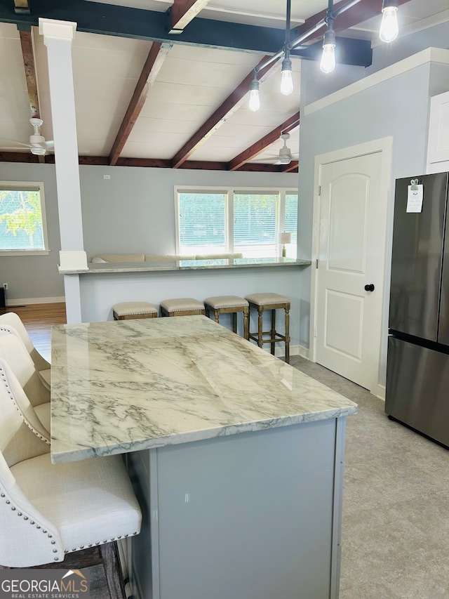 kitchen with a breakfast bar area, stainless steel refrigerator, light carpet, and a healthy amount of sunlight