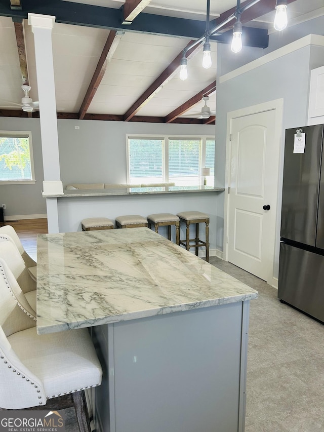 kitchen featuring white cabinetry, beam ceiling, stainless steel fridge, and a breakfast bar