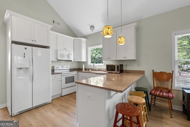 kitchen featuring white appliances, white cabinetry, a kitchen breakfast bar, hanging light fixtures, and kitchen peninsula