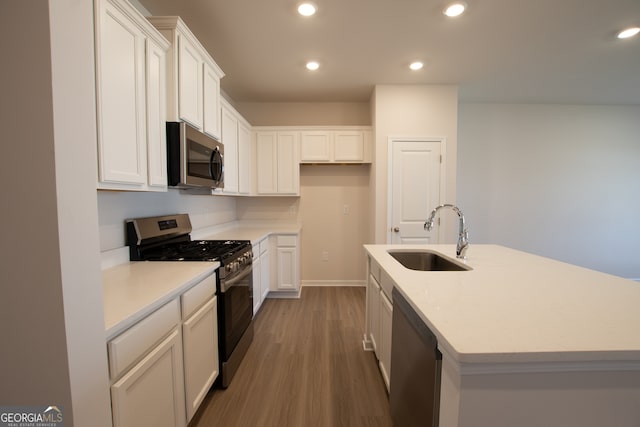 kitchen featuring sink, wood-type flooring, an island with sink, stainless steel appliances, and white cabinets