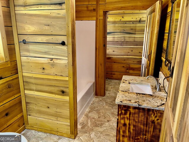 bathroom with a washtub, vanity, and wood walls