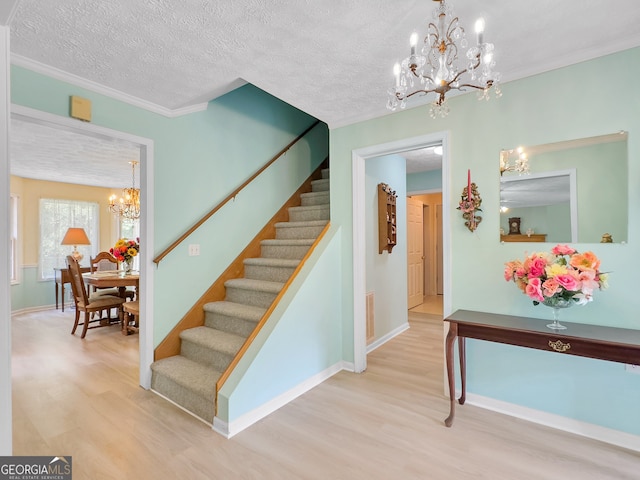 stairs with an inviting chandelier, hardwood / wood-style flooring, ornamental molding, and a textured ceiling