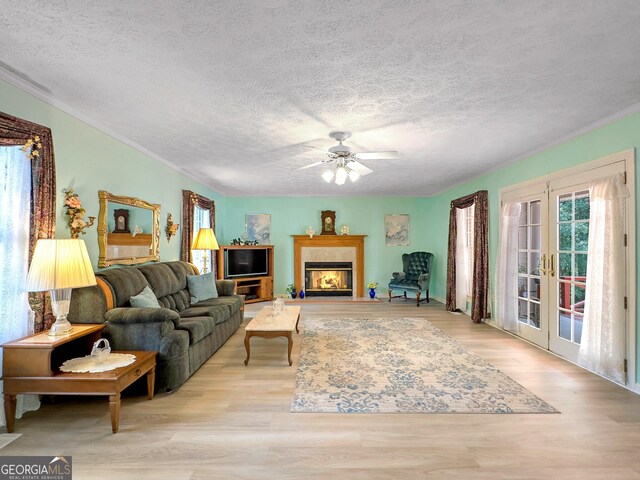 living room with french doors, light wood-type flooring, a textured ceiling, ceiling fan, and ornamental molding