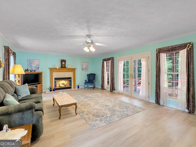 living room featuring ceiling fan, light hardwood / wood-style floors, french doors, and a textured ceiling