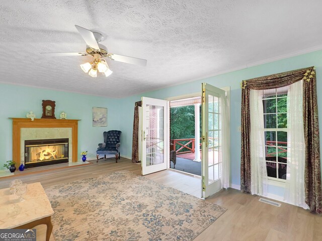 unfurnished living room with ceiling fan, french doors, light hardwood / wood-style floors, a premium fireplace, and a textured ceiling