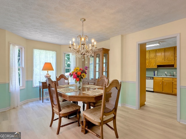 dining space with sink, a chandelier, light wood-type flooring, and a textured ceiling