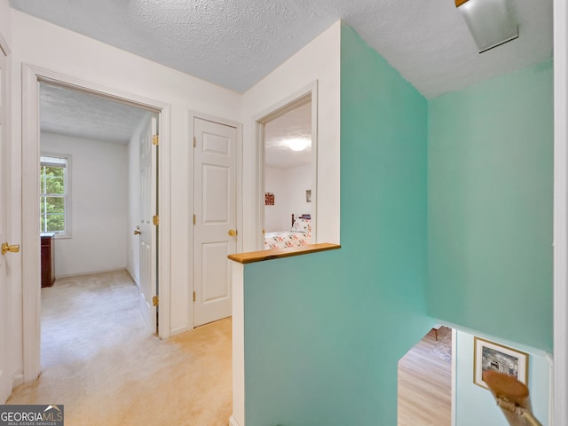 hallway with light carpet and a textured ceiling