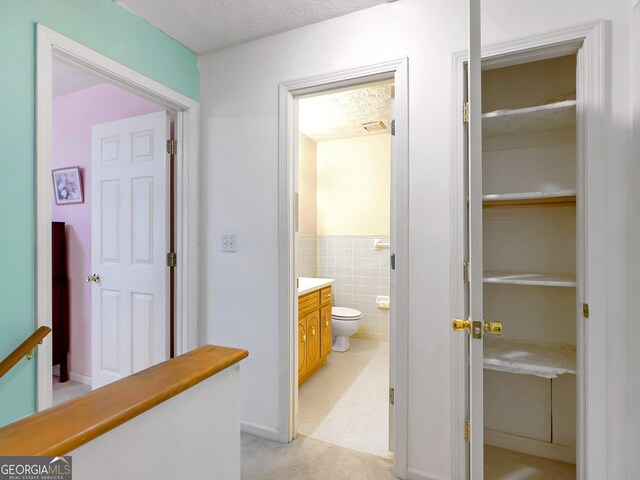 corridor featuring tile walls, light carpet, and a textured ceiling