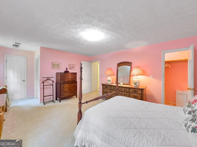 bedroom with a spacious closet, light carpet, a closet, and a textured ceiling