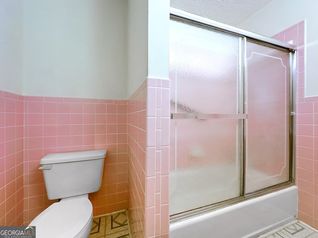 bathroom featuring toilet, tile patterned floors, enclosed tub / shower combo, and tile walls