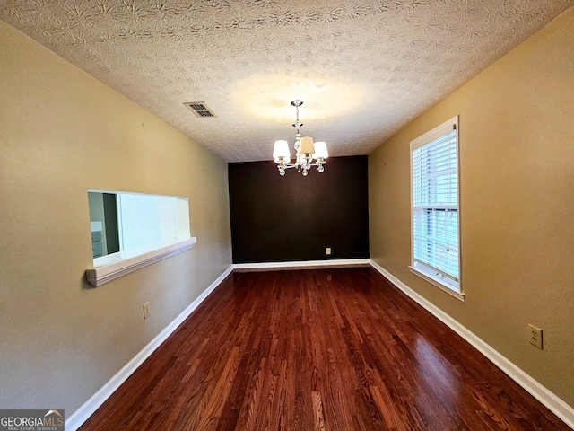 empty room with an inviting chandelier, hardwood / wood-style flooring, and a textured ceiling