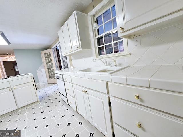 kitchen featuring tile counters, white cabinets, backsplash, sink, and light tile floors