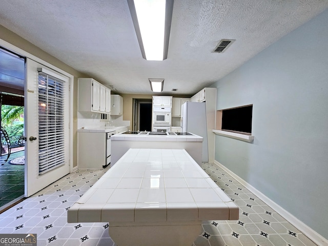 kitchen with kitchen peninsula, white appliances, white cabinetry, and tile counters