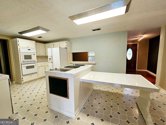 kitchen with white appliances, white cabinets, kitchen peninsula, tile countertops, and light tile flooring