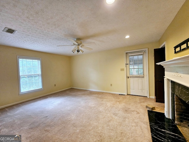 unfurnished living room featuring a textured ceiling, ceiling fan, a high end fireplace, and carpet floors