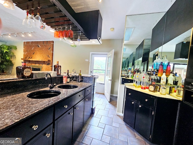 kitchen featuring sink, dark stone countertops, light tile floors, and rail lighting