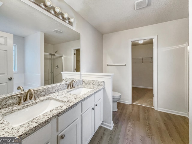 bathroom with wood-type flooring, a textured ceiling, toilet, a shower with door, and vanity