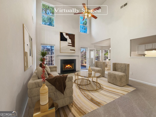 carpeted living room with ceiling fan and a high ceiling