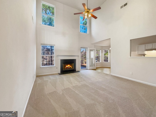 unfurnished living room with ceiling fan, light colored carpet, and a high ceiling