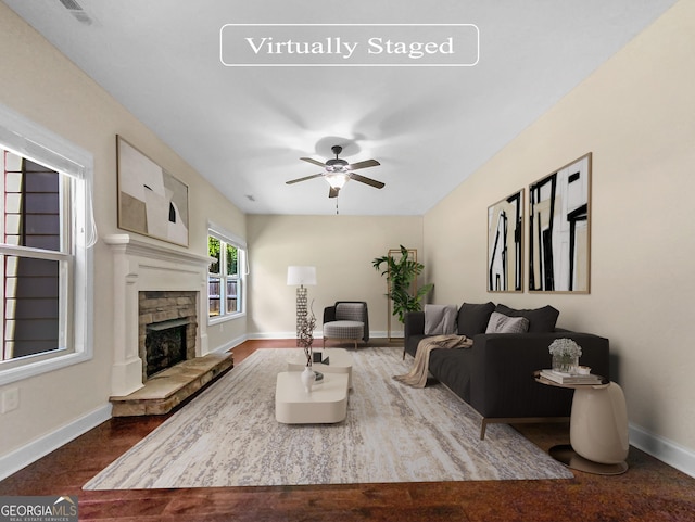 living room featuring hardwood / wood-style flooring, ceiling fan, and a stone fireplace