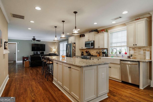 kitchen with sink, light stone counters, decorative light fixtures, a kitchen island, and stainless steel appliances