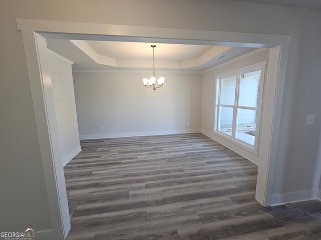 unfurnished dining area with wood-type flooring, ornamental molding, an inviting chandelier, and a tray ceiling