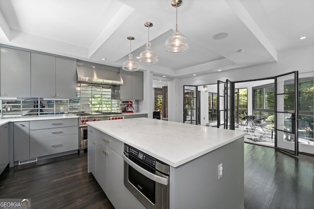 kitchen featuring decorative light fixtures, a kitchen island, a tray ceiling, wall chimney exhaust hood, and gray cabinets