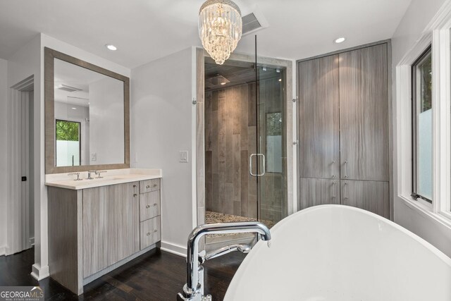 bathroom featuring a notable chandelier, wood-type flooring, vanity with extensive cabinet space, and plus walk in shower