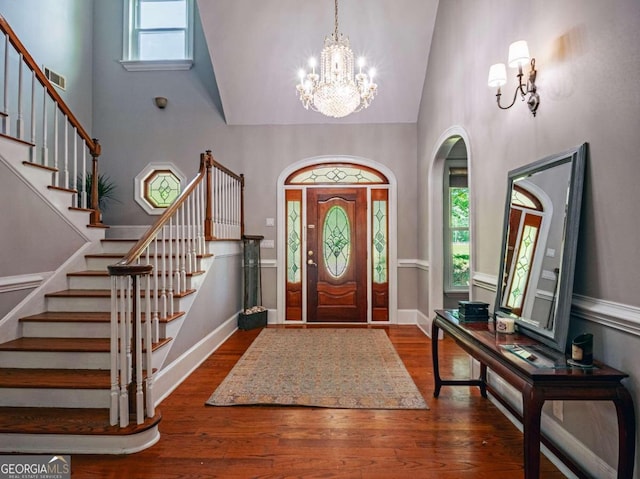 entryway with an inviting chandelier, high vaulted ceiling, and dark wood-type flooring