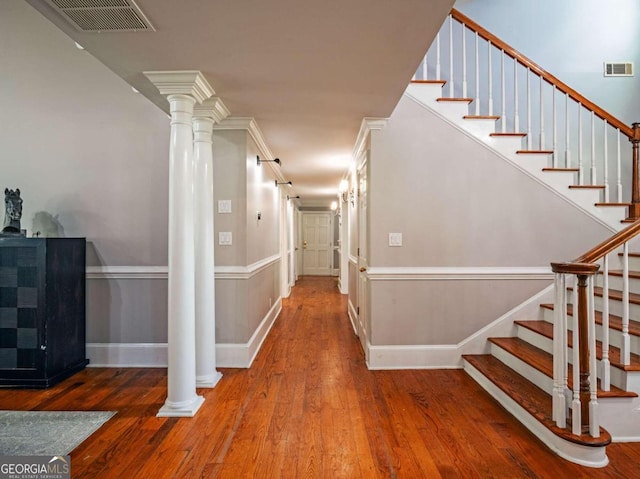 stairs with decorative columns, wood-type flooring, and ornamental molding