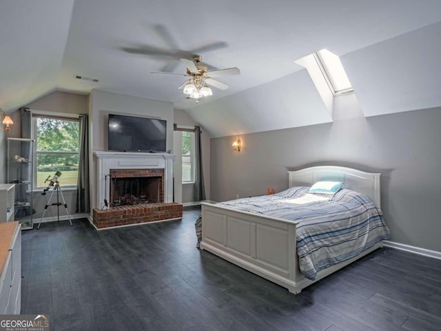 bedroom featuring a fireplace, dark hardwood / wood-style floors, lofted ceiling with skylight, and ceiling fan