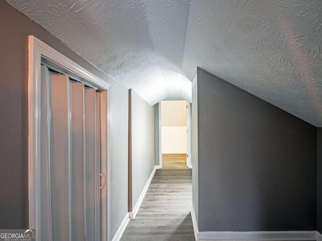 corridor featuring wood-type flooring, a textured ceiling, and vaulted ceiling