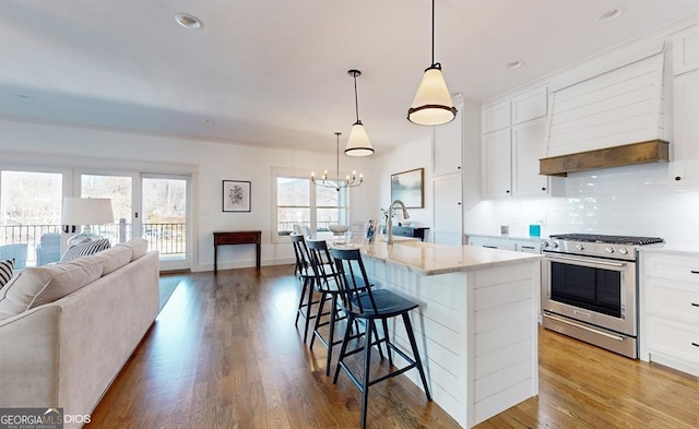 kitchen with stainless steel gas stove, hanging light fixtures, a breakfast bar area, a center island with sink, and white cabinets