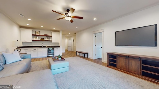 living room featuring ceiling fan, light hardwood / wood-style floors, ornamental molding, and beverage cooler