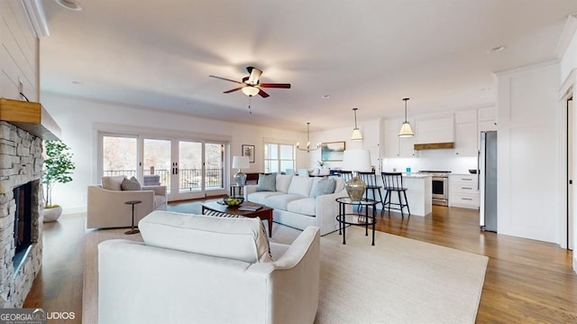 living room with ceiling fan with notable chandelier, light hardwood / wood-style floors, and a stone fireplace