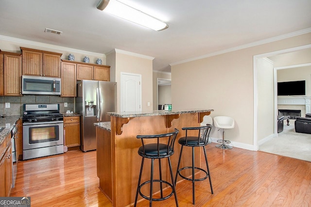 kitchen featuring appliances with stainless steel finishes, a kitchen island, ornamental molding, and a breakfast bar area