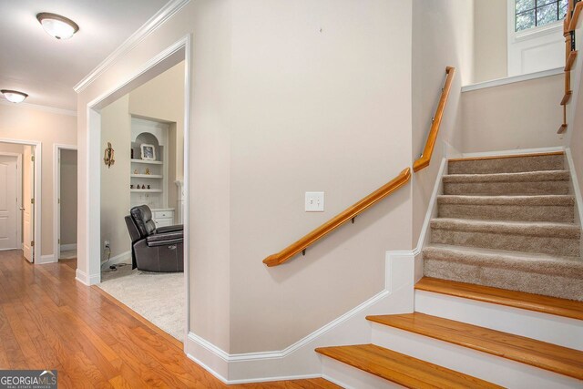 staircase with wood-type flooring and ornamental molding