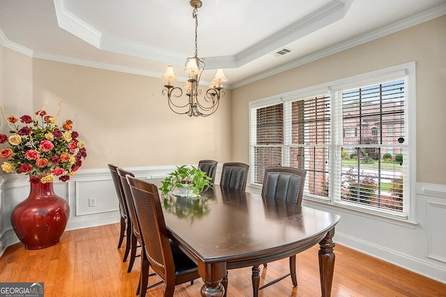 dining space featuring a raised ceiling, ornamental molding, and light hardwood / wood-style flooring