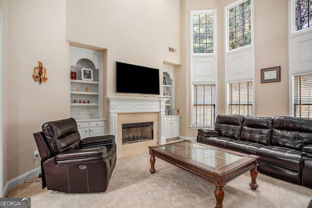 living room featuring built in shelves, a premium fireplace, light carpet, and a high ceiling