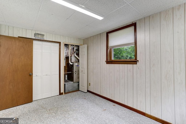 unfurnished bedroom with light carpet, a paneled ceiling, and wood walls