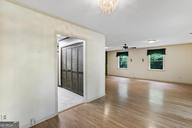 spare room with ceiling fan with notable chandelier, a textured ceiling, and light hardwood / wood-style floors