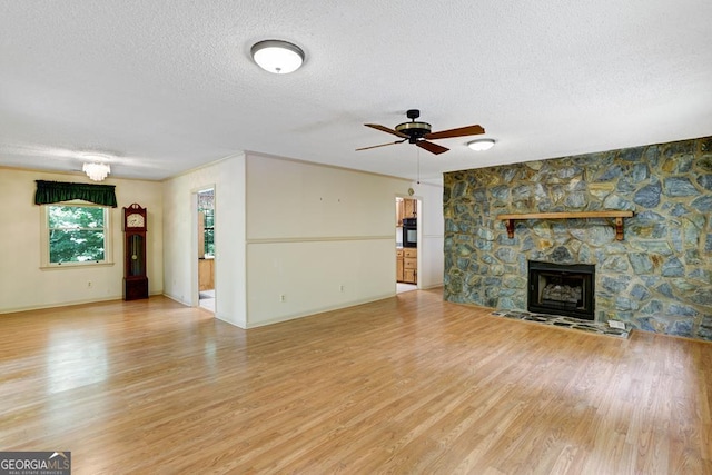 unfurnished living room featuring hardwood / wood-style floors, a textured ceiling, a stone fireplace, and ceiling fan