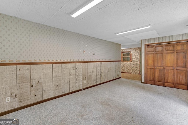 empty room featuring carpet, a paneled ceiling, and wood walls