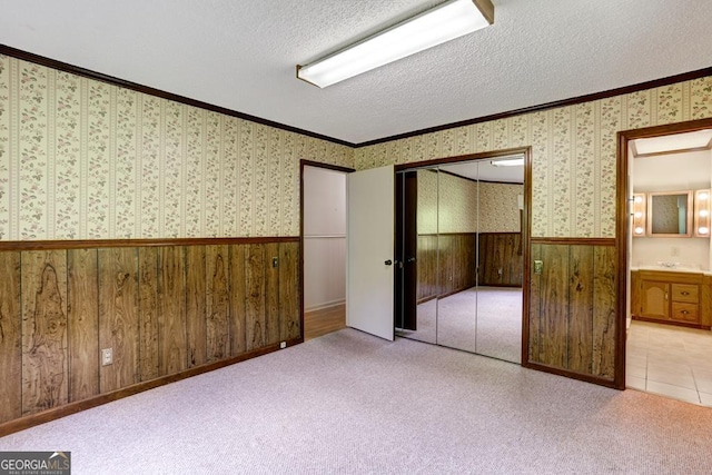 unfurnished bedroom featuring a textured ceiling, light colored carpet, a closet, and ornamental molding