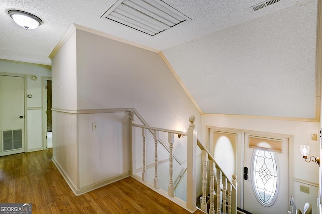 entryway featuring hardwood / wood-style flooring, crown molding, a textured ceiling, and vaulted ceiling