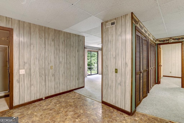 corridor featuring a drop ceiling, light carpet, and wooden walls