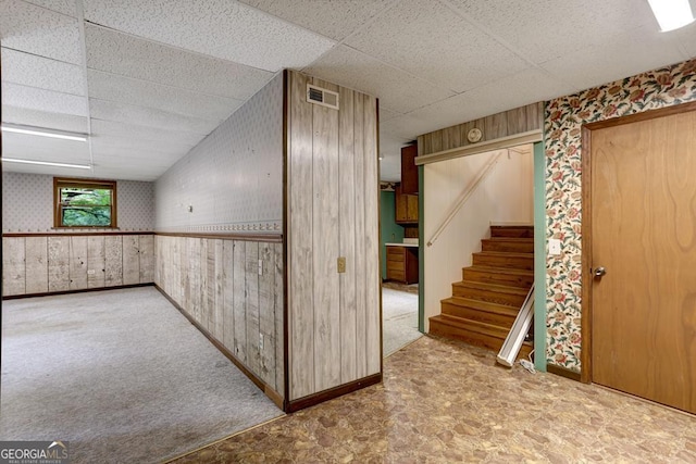 basement featuring carpet flooring, a paneled ceiling, and wooden walls